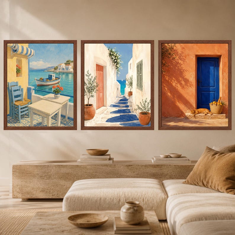 May include: A set of three framed wall art prints featuring Mediterranean scenes. The first shows a coastal view with a boat, the second a sunlit alleyway with potted plants, and the third an orange wall with a blue door and a resting cat.