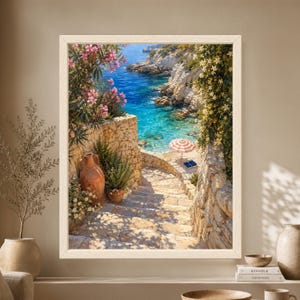 Framed Mediterranean coastal wall art showing sunlit stone stairs descending to a turquoise rocky cove with pink flowers, terracotta pots and a striped beach umbrella beside the sea.