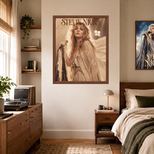Może przedstawiać: Oprawiony plakat ścienny przedstawiający fotografię w odcieniach sepii, na kt&oacute;rej Stevie Nicks ma długie, falowane włosy, ubrana jest w str&oacute;j z frędzlami i trzyma mikrofon. Nazwisko Stevie Nicks jest wydrukowane stylizowaną brązową czcionką szeryfową.