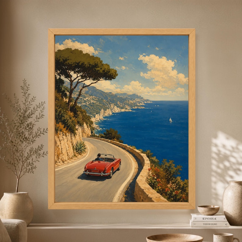 Framed Amalfi Coast wall art showing a red vintage convertible driving along a winding Mediterranean cliff road above deep blue sea, sailboats and an Italian coastal landscape.