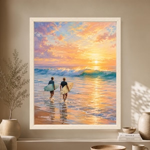 Framed surfer sunset wall art showing two surfers carrying blue and cream surfboards into glowing ocean waves beneath a colorful peach, gold and lavender evening sky.