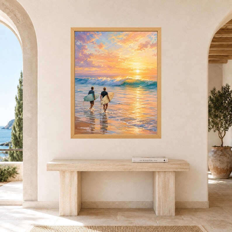 May include: A framed wall art print depicting two individuals carrying surfboards into the ocean at sunset. The scene features a vibrant orange and yellow sky reflecting on the water, with a breaking wave and a sandy beach in the foreground.