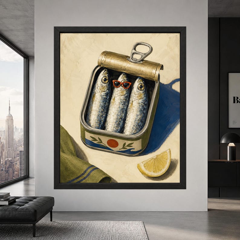 Framed sardine tin wall art showing three silver sardines inside an open can, with the middle fish wearing red sunglasses beside a lemon wedge on a cream, blue and olive background.