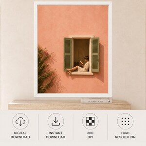 May include: A framed wall art print featuring a peach-colored stucco wall with a window. The window has open sage green shutters and shows a person sitting inside reading a book. A green climbing plant grows along the left side of the wall.