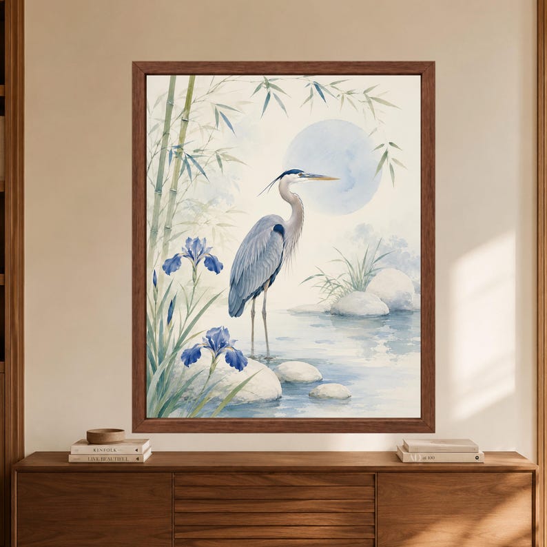 Framed Japanese heron wall art showing a blue gray heron standing in shallow water among blue iris flowers, bamboo, pale stones and a soft blue moon in a minimalist watercolor scene.