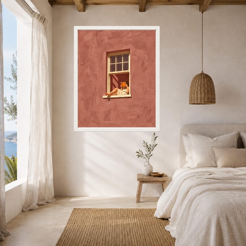 May include: A framed wall art print featuring a textured terracotta-colored wall with a single window. A person sits in the window frame reading an orange book. The artwork is displayed in a white frame and hangs on a neutral-toned bedroom wall.