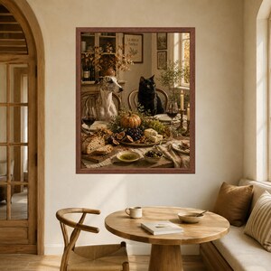 Op de afbeelding: Een ingelijste kunstdruk met een grijs-witte whippet en een zwarte kat aan een eettafel gedekt met een pompoen, druiven, vijgen, kaas, brood, olijven en wijnglazen. De sc&egrave;ne speelt zich af in een rustiek interieur van een eetkamer.