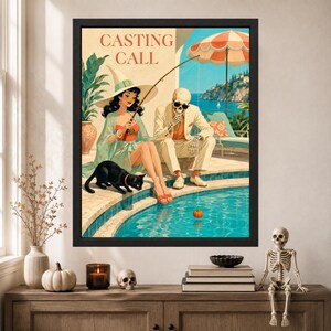 May include: A framed wall art print titled CASTING CALL featuring a witch in a light green robe and hat sitting by a pool with a skeleton in a beige suit. A black cat sits nearby while they fish for a small orange pumpkin in the blue water.
