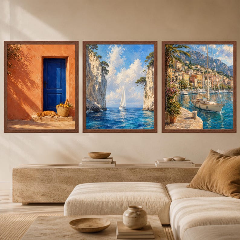 May include: A set of three framed wall art prints. The left print shows a blue door on an orange wall with a cat and basket. The center print depicts a sailboat between cliffs on blue water. The right print shows a harbor with a boat and buildings.
