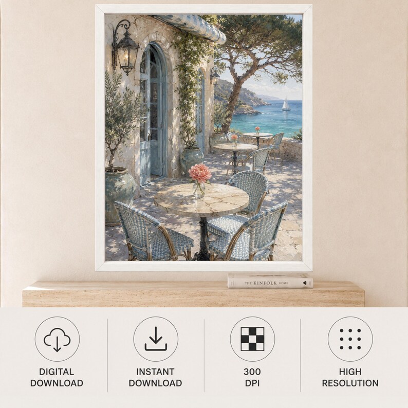May include: A framed wall art print depicting a Mediterranean terrace scene with stone arches, blue-toned wicker chairs, and round tables. A vase with pink flowers sits on a table, while a view of the sea with a sailboat is visible in the distance.