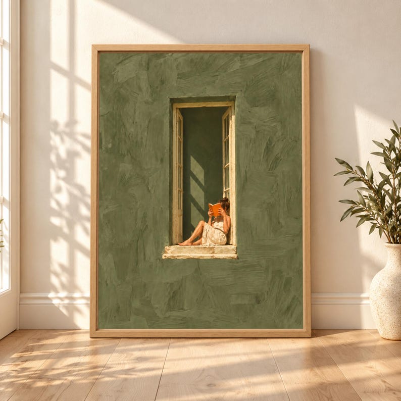 Framed olive green wall art showing a barefoot woman reading an orange book while sitting in a tall open cream window against a textured minimalist green wall.