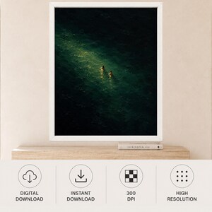 May include: A framed wall art print featuring a dark, deep green ocean scene with two small figures swimming in a bright, narrow shaft of light that cuts diagonally across the water, creating a high-contrast visual of light and shadow.