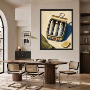 May include: A framed wall art print depicting an open metal tin of three sardines, with the center fish wearing small red-rimmed sunglasses. A slice of yellow lemon and a folded green cloth with blue stripes sit beside the tin on a light background.
