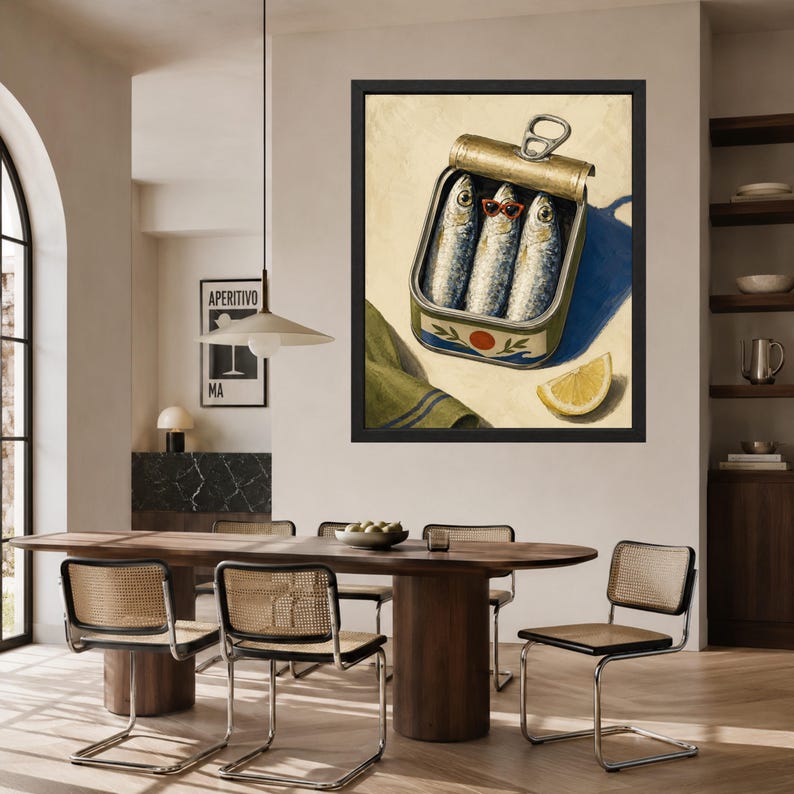 May include: A framed wall art print depicting an open metal tin of three sardines, with the center fish wearing small red-rimmed sunglasses. A slice of yellow lemon and a folded green cloth with blue stripes sit beside the tin on a light background.