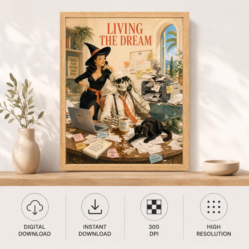 May include: A framed wall art print titled LIVING THE DREAM featuring a witch in a black dress and hat standing beside a skeleton wearing a tie and sunglasses at a desk. A black cat sits on a cluttered desk with a laptop, phone, and papers.