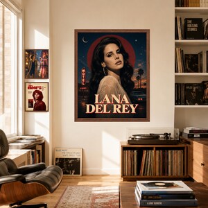 Puede incluir: Un p&oacute;ster de pared enmarcado que presenta un retrato de Lana Del Rey sobre un fondo de atardecer oscuro con un letrero de motel, palmeras y un coche. El texto LANA DEL REY est&aacute; impreso en letras grandes, negritas y de color crema abajo.