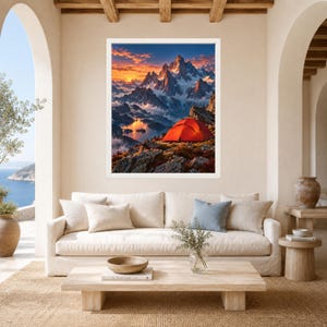 May include: A framed wall art print depicting a vibrant mountain landscape at sunset. A bright orange tent sits on a rocky foreground overlooking a calm lake nestled between snow-capped peaks under a sky filled with orange and blue clouds.