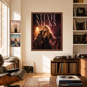 May include: A framed wall poster featuring a photograph of Stevie Nicks performing on stage with long blonde hair and a black fringed outfit. The text STEVIE NICKS is printed in large white letters at the top, with smaller text on the right side.