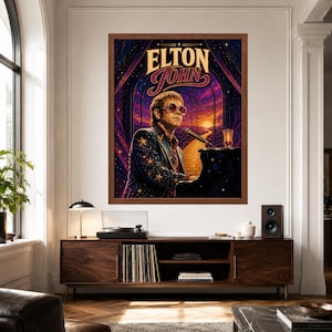 May include: A framed wall art print featuring a stylized illustration of Elton John playing a black piano. The artwork displays a starry night sky, a yellow brick road leading to a sunset, and the text ELTON JOHN in bold, decorative lettering.