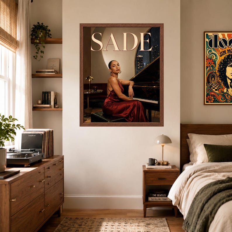 May include: A framed wall poster featuring a portrait of Sade sitting at a grand piano. The singer wears a sleeveless, floor-length, dark red satin dress. The word SADE is printed in large, light-colored capital letters at the top of the image.