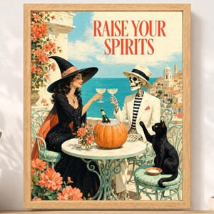 May include: A framed art print featuring a witch in a black dress and a skeleton in a white suit sitting at a table with a pumpkin, clinking glasses. The text RAISE YOUR SPIRITS is at the top. A black cat sits on a chair near a coastal town.