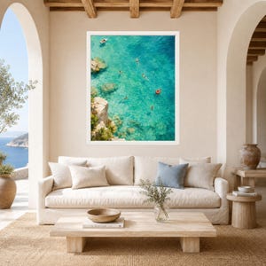 Puede incluir: Una impresi&oacute;n de arte mural enmarcada que muestra una vista a&eacute;rea de agua de mar turquesa con acantilados rocosos a la izquierda. Varias personas nadan en el agua clara y una persona flota con un anillo de nataci&oacute;n circular naranja.