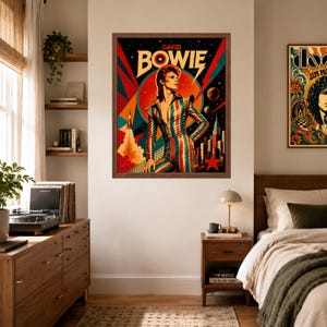 May include: A framed wall art print featuring a stylised illustration of David Bowie in a striped jumpsuit against a cosmic background with a rocket, planets, and city skyline. The text DAVID BOWIE is printed in bold yellow letters at the top.