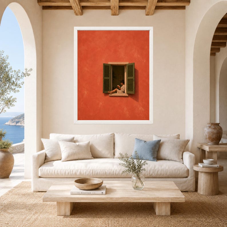 May include: A framed wall art print featuring a vibrant orange wall with an open window. A person sits on the window ledge reading a book. The window has dark green shutters on either side. The artwork is displayed in a white frame.