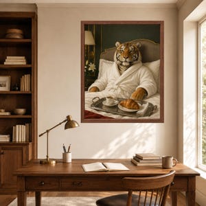 May include: A framed wall art print depicting a tiger wearing a white plush bathrobe, sitting upright in a bed with white pillows. A silver tray rests on the bed, holding a white ceramic cup of coffee and a golden-brown croissant on a small plate.