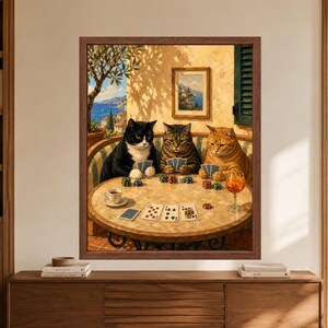 Framed cats playing poker wall art showing three cats holding cards around a table with poker chips, espresso and an orange drink on a sunny Mediterranean coastal terrace.