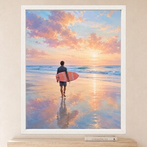 May include: A framed wall art print depicting a person walking on a wet sandy beach at sunset while carrying a coral-colored surfboard. The scene features a calm ocean, soft pastel clouds in shades of pink and orange, and a reflection on the sand.