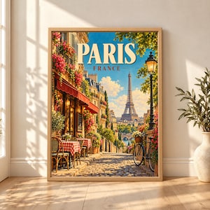 Framed Paris France travel poster showing the Eiffel Tower beyond a flower-lined cobblestone street with red café awnings, outdoor tables, a black bicycle and classic Parisian street lamps.