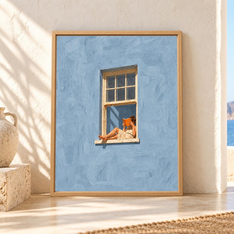 Framed soft blue wall art showing a barefoot woman sitting in an open cream window while reading an orange book against a textured minimalist blue wall.
