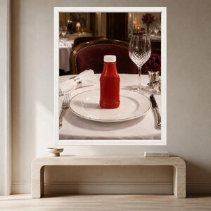 May include: A red plastic squeeze bottle with a white cap sits centered on a white ceramic dinner plate. The place setting includes a silver fork to the left, a silver knife to the right, a folded white napkin, and a clear crystal wine glass.