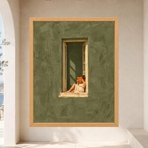 May include: A framed wall art print featuring a textured olive green wall with a central open window. A figure in a light-colored dress sits in the window frame reading an orange book, with sunlight casting distinct shadows across the scene.