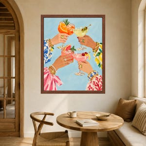 May include: A framed wall art print depicting four hands raised in a toast, each holding a different cocktail glass filled with colorful drinks garnished with fruit slices and olives, set against a light blue background with patterned sleeves.