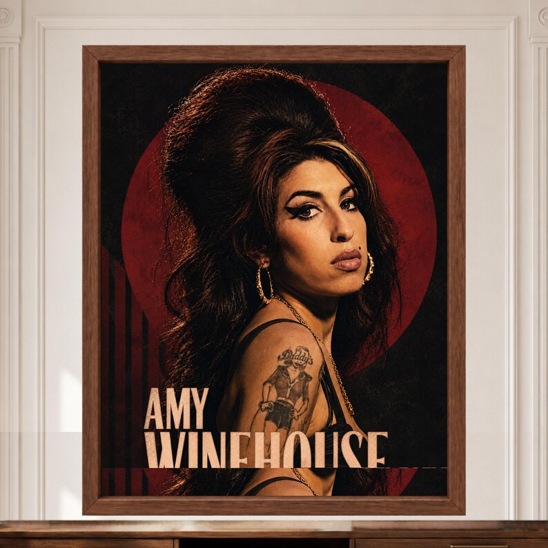 Puede incluir: Un retrato impreso y enmarcado de Amy Winehouse con su caracter&iacute;stico peinado de colmena, delineador de ojos alado y pendientes de aro dorados. El fondo es un c&iacute;rculo rojo oscuro sobre negro, con el texto AMY WINEHOUSE en blanco.