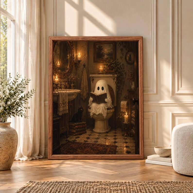 Framed gothic Halloween bathroom wall art showing a sheet ghost reading a book on a toilet beside a black cat in a candlelit vintage bathroom with dark wood and antique decor.