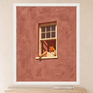 May include: A framed wall art print featuring a textured, terracotta-colored wall with a single window. A person sits in the window frame, wearing a light-colored dress and reading an orange book. The artwork is enclosed in a simple white frame.
