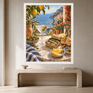 May include: A framed wall art print depicting a coastal scene with a martini glass, a bowl of green olives, a tin of sardines, lemon slices, and bread on a marble table. The background features a blue sea, cliffs, and buildings under a bright sky.