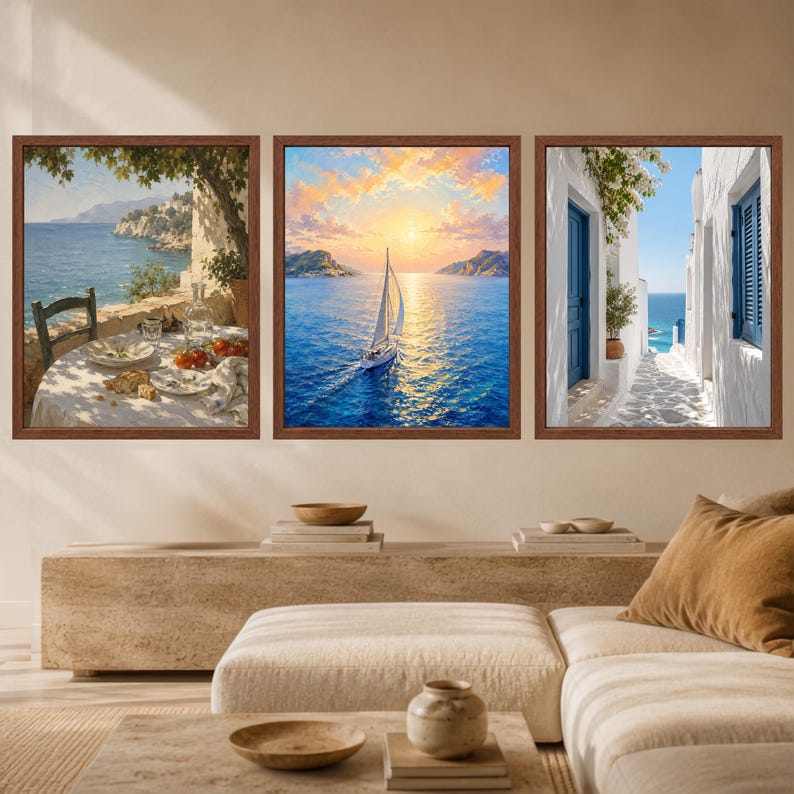 May include: A set of three framed wall art prints featuring coastal scenes. The left print shows a table set for a meal overlooking the sea. The center print depicts a sailboat on blue water at sunset. The right print shows a white alleyway.