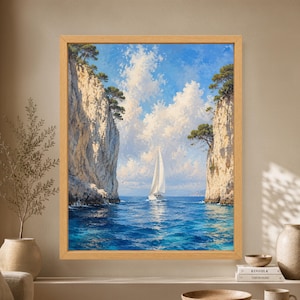 Framed Mediterranean sailboat wall art showing a white sailing yacht on bright blue water between tall limestone cliffs topped with pine trees beneath large sunlit clouds.