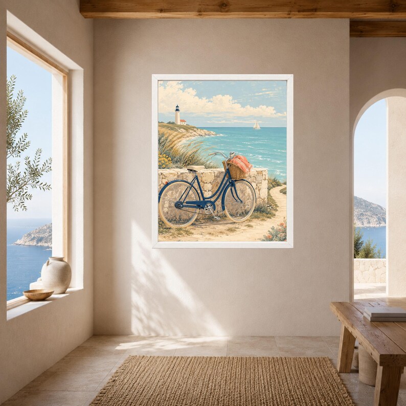 Op de afbeelding: Een ingelijste muurkunstprint met een donkerblauwe fiets met een rieten mand vol roze bloemen, geparkeerd tegen een stenen muur op een kustpad. Op de achtergrond staat een witte vuurtoren op een klif die uitkijkt over de blauwe oceaan.