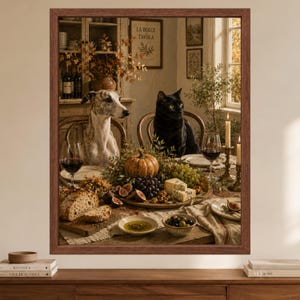 Op de afbeelding: Een ingelijste kunstdruk met een gestroomde windhond en een zwarte kat aan een eettafel gedekt met een feestmaal van brood, druiven, vijgen, kaas, een pompoen en wijnglazen, met de tekst LA DOLCE TAVOLA zichtbaar op een bord aan de muur.