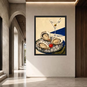 May include: A framed wall art print featuring three raw oysters served on a bed of crushed ice on a plate, accompanied by a martini glass with a single green olive and a bright red cherry placed next to the oysters on a blue and yellow surface.