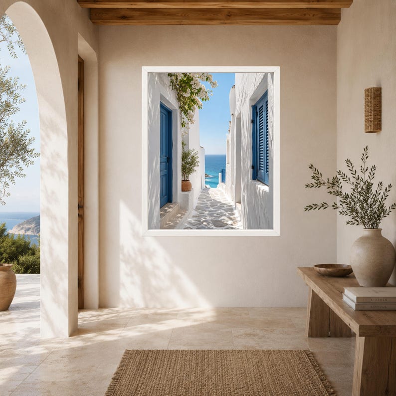 K&ouml;nnte beinhalten: Ein gerahmter Kunstdruck, der eine schmale mediterrane Gasse mit wei&szlig;en Stuckw&auml;nden, leuchtend blauen T&uuml;ren und Fensterl&auml;den, einer Topfpflanze und einem Steinweg zeigt, der unter klarem Himmel zu einem hellblauen Meer f&uuml;hrt.