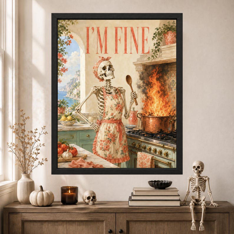 May include: A framed wall art print featuring a skeleton wearing a floral apron and headscarf, standing in a kitchen with a large pot of fire on the stove. The text I'M FINE is printed in red at the top. The scene includes a coastal window view.