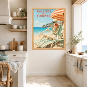 May include: A framed wall art print featuring a skeleton wearing sunglasses and a red scarf, lounging on a beach chair under a red and white striped umbrella. The text TAN LINES ARE FOREVER is printed above the skeleton, with a blue ocean background.
