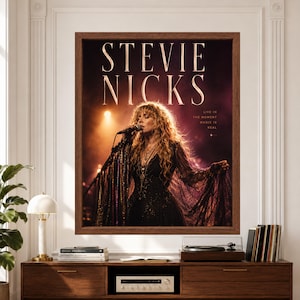 Framed music poster labeled Stevie Nicks showing a female rock singer performing at a microphone in a flowing black lace dress under warm amber and purple concert lights.