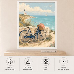 Op de afbeelding: Een ingelijste kunstdruk met een blauwe fiets met een rieten mand met een koraalkleurige doek, geparkeerd tegen een stenen muur. Op de achtergrond staat een vuurtoren op een met gras begroeide klif die uitkijkt over een blauwe oceaan.